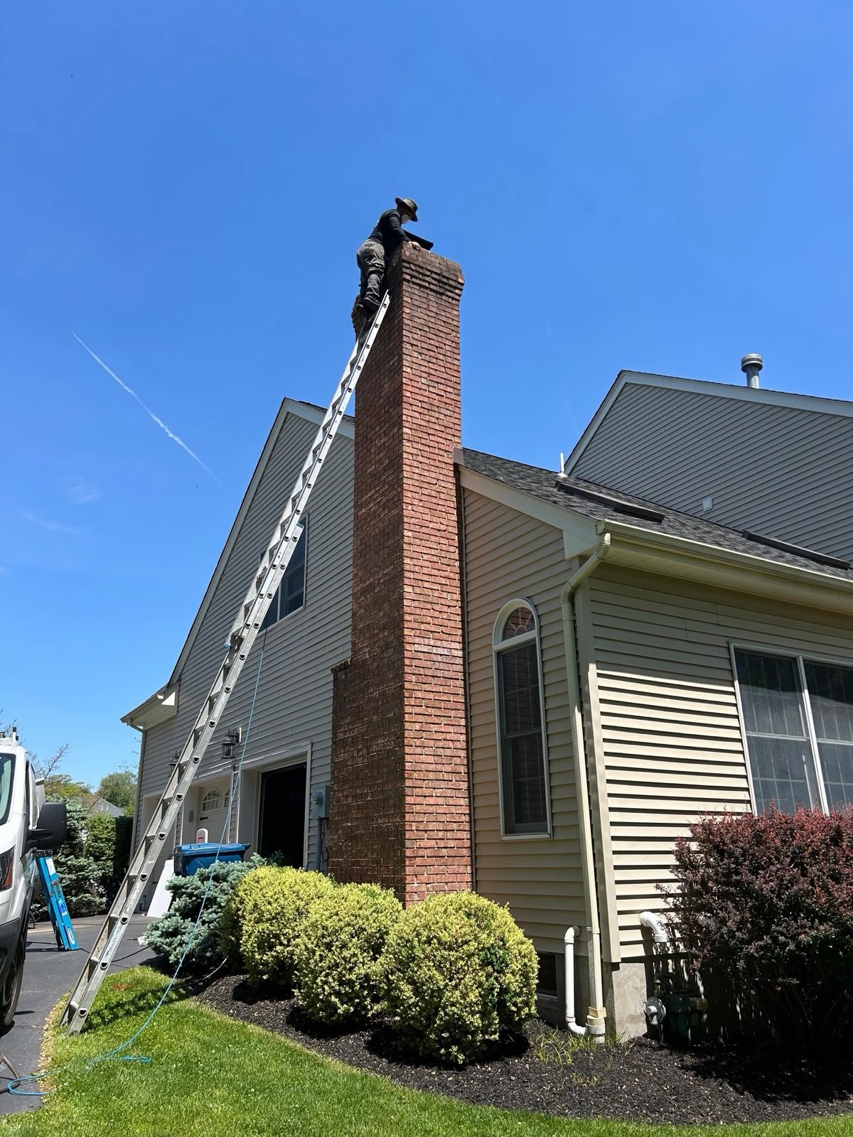 A technician working on a tall brick chimney beside a home