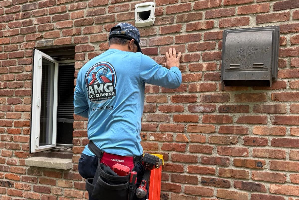AMG technician in a blue uniform working at an exterior wall vent
