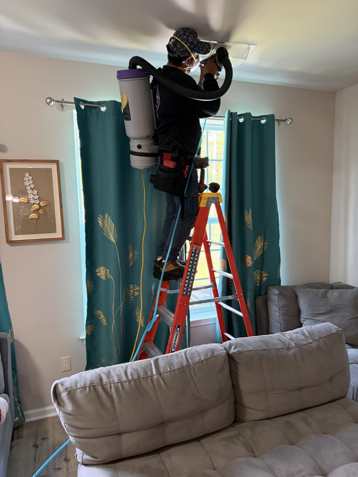 An AMG technician cleaning a ceiling vent from a ladder