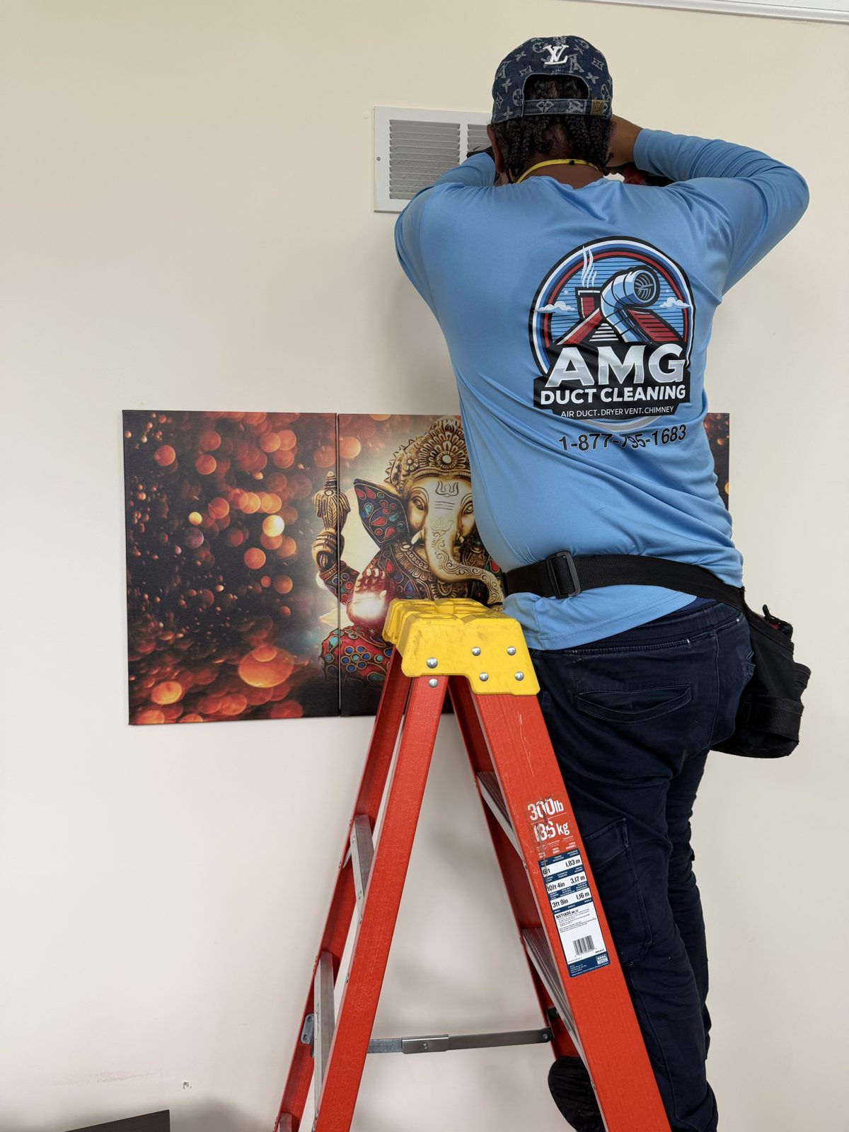 An AMG technician cleaning a wall vent from a ladder