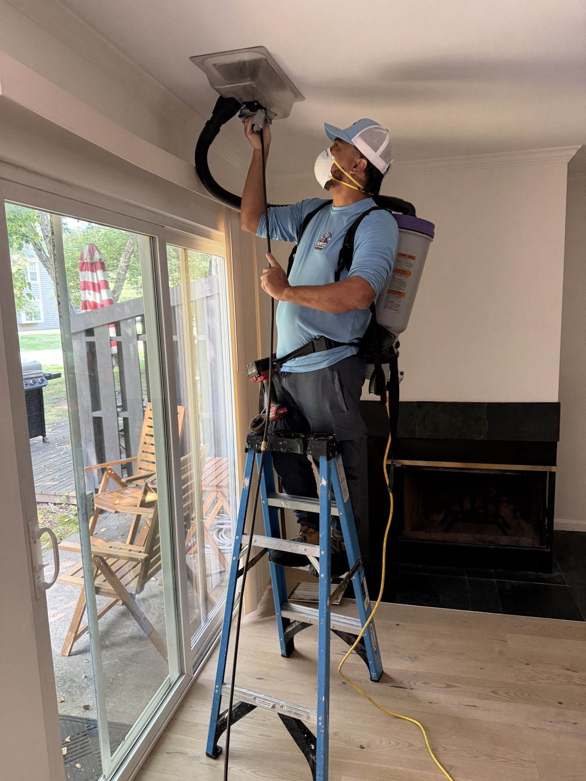 An AMG technician cleaning a ceiling vent with a HEPA vacuum