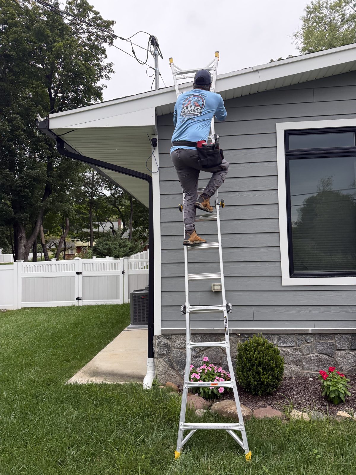 An AMG technician on a ladder servicing an exterior vent