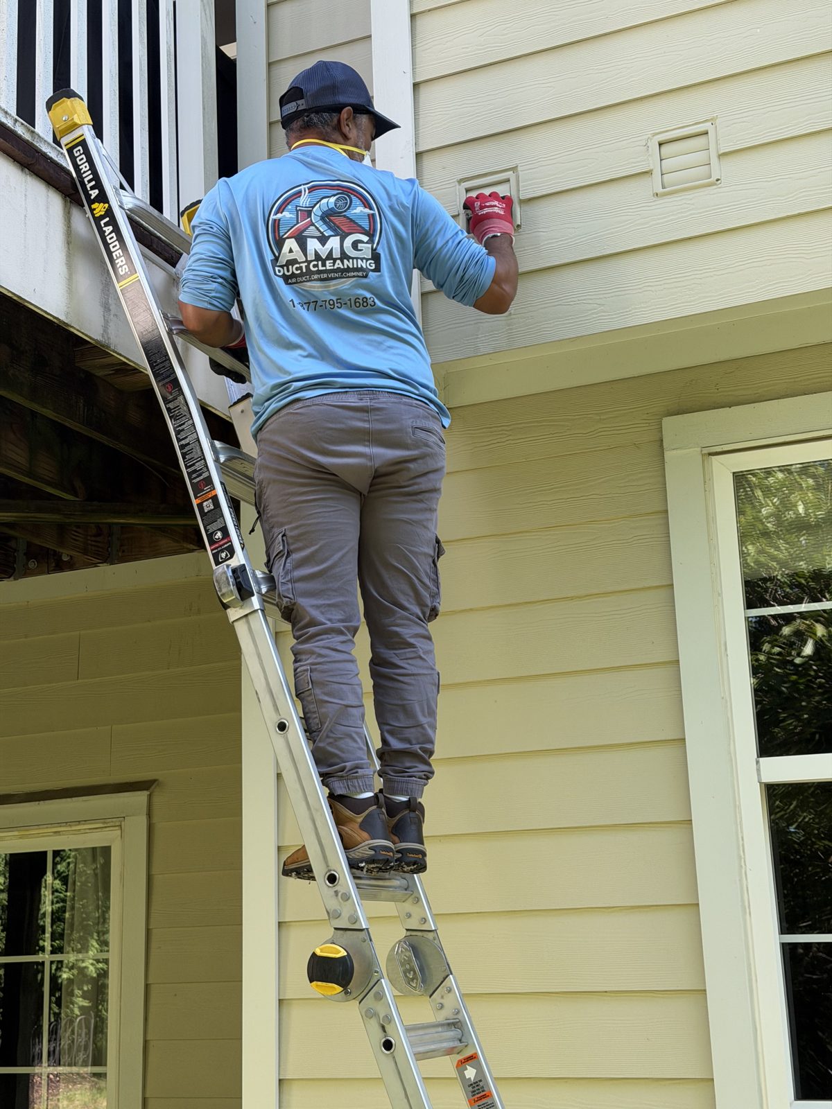 An AMG technician on a ladder at a home exterior